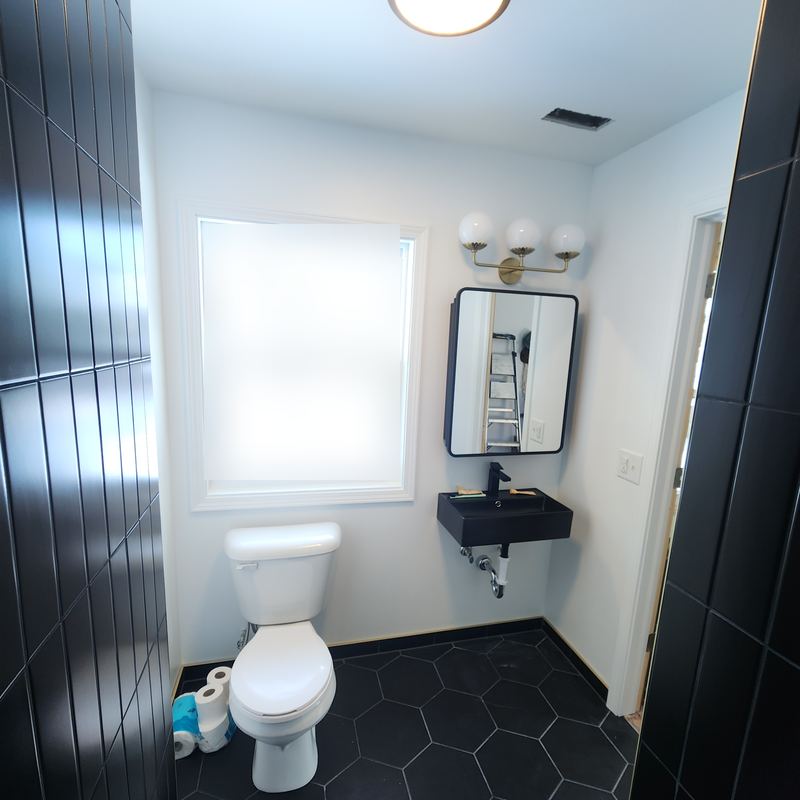 The same wall finished: white walls, black floating sink, round mirror, black hex tile floor