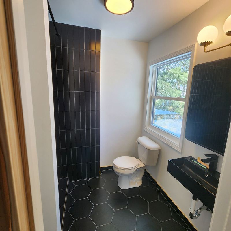 The shower side finished with black vertical tile and a black hex floor