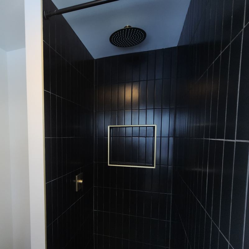 Walk-in shower in black vertical tile with a rain head and a recessed niche
