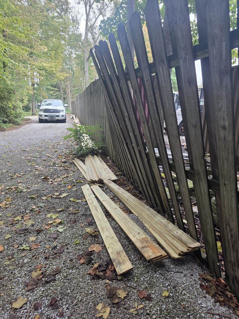 A wooden privacy fence leaning badly, loose boards on the gravel