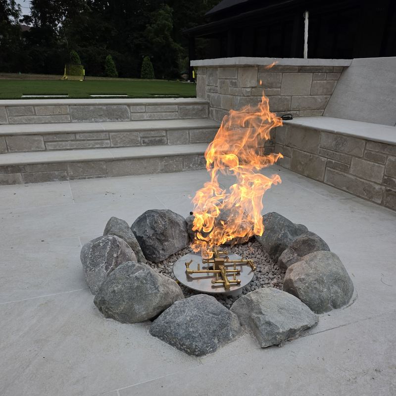 A gas fire feature burning in a ring of boulders on a stone patio