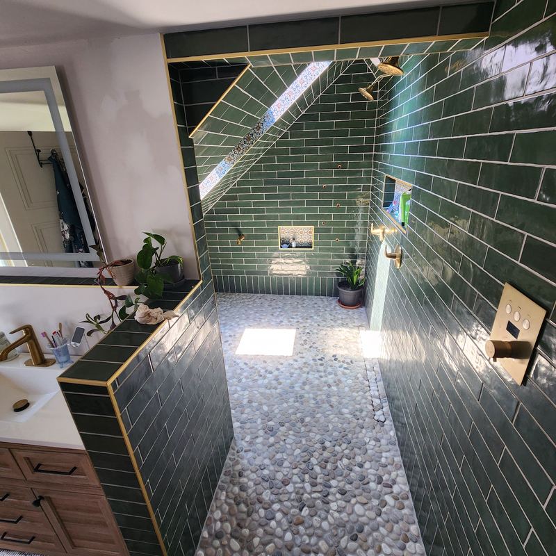 The finished bathroom: green subway-tile shower, pebble floor, brass fixtures, wood vanity
