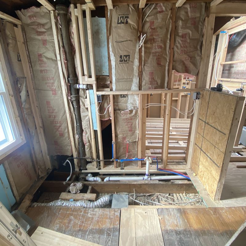 A bathroom stripped to the framing: open studs, insulation, exposed plumbing