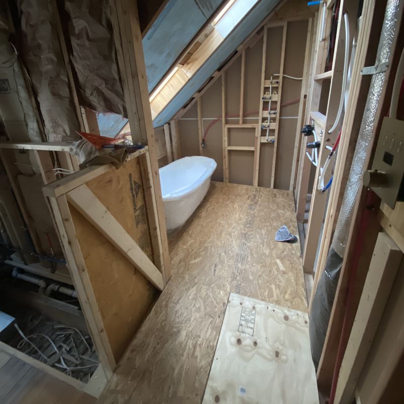 New framing and subfloor under the sloped ceiling, the tub still wrapped in plastic