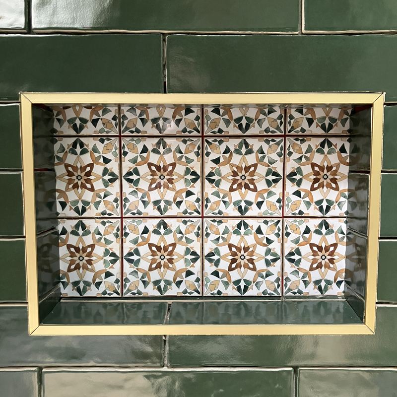 A shower niche lined with patterned tile and trimmed in brass