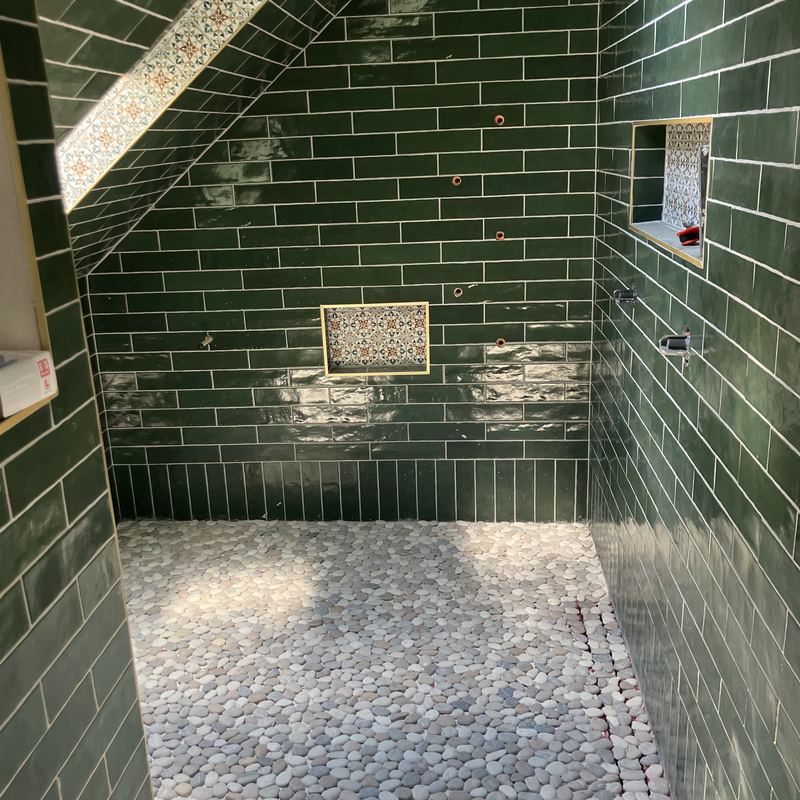 The finished shower under the slope: green subway tile, pebble floor, patterned tile niche