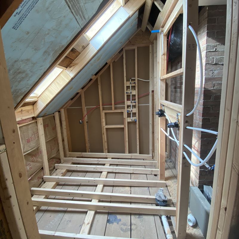 The shower area framed under a sloped ceiling, plumbing roughed in